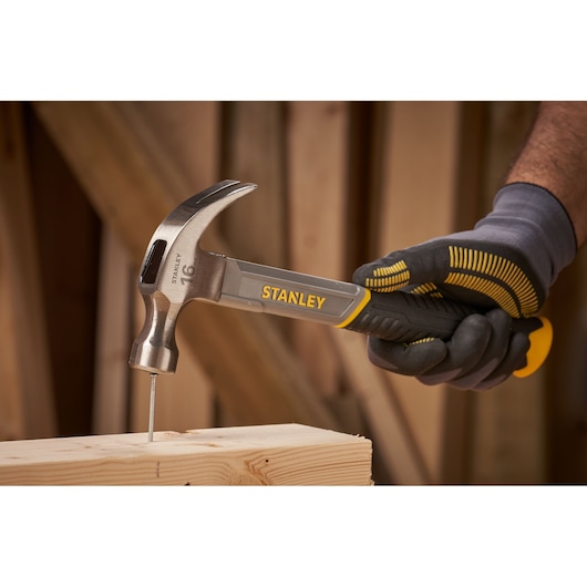 Photo of STANLEY STHT0-51309 claw hammer driving a nail into wood, held in a gloved hand.