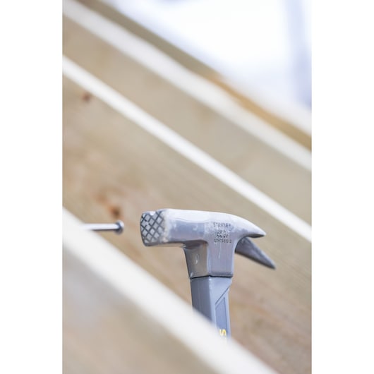 STANLEY STHT0-51312 hammer with textured head, shown in a construction setting with wood beams.