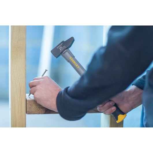 Photo of STANLEY STHT0-54129 hammer driving nail into wooden beam, close-up of worker’s hands.