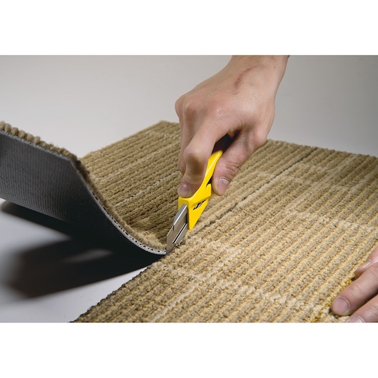 STANLEY STHT10265-0 utility knife cutting beige carpet, close-up hand use, product photography.