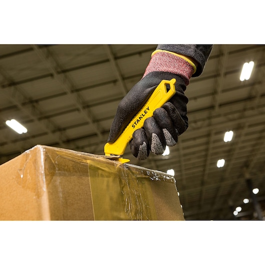 Stanley STHT10355-1 yellow safety utility knife used to cut box tape, close-up photography.