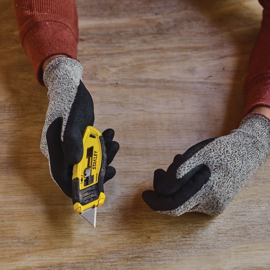 Photo of STANLEY STHT10432-0 utility knife held in gloved hand on wooden surface.