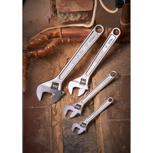 Photo of STANLEY STHT13121-0 adjustable wrenches set in four sizes on a dusty tile and pipe background.