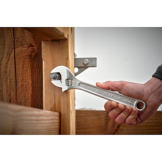 STANLEY STHT13123-0 adjustable wrench used on a bolt in wooden structure, close-up photography.