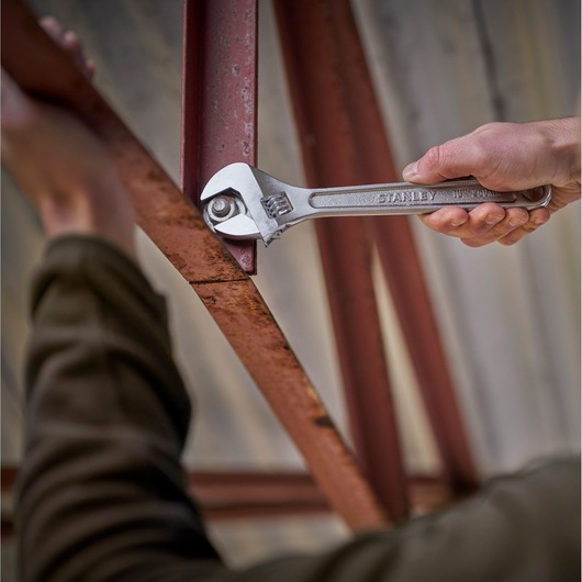 Stanley STHT13123-0 adjustable wrench in use tightening a bolt on a rusted metal beam, close-up view.