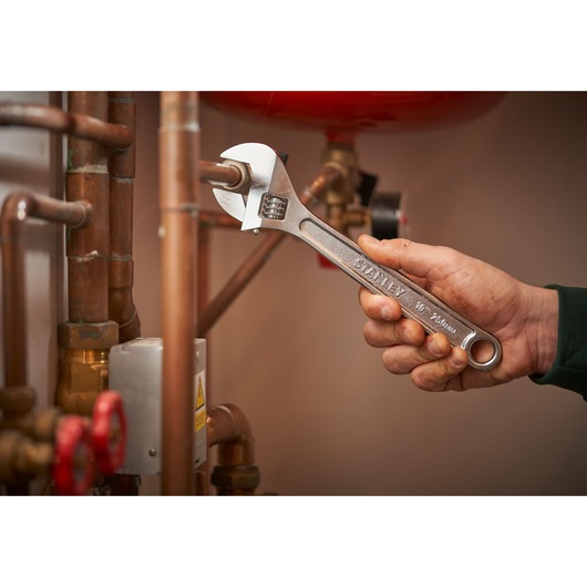 Stanley STHT13156-0 adjustable wrench used on copper pipes, close-up of tool in hand.