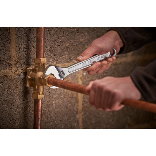 STANLEY STHT13156-0 adjustable wrench being used to tighten a copper pipe fitting against a masonry wall.
