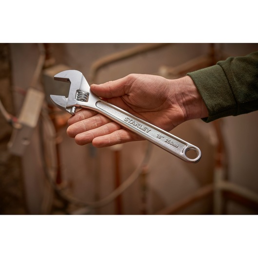 Photo of STANLEY STHT13156-0 adjustable wrench, 250mm, held in hand with background of copper pipes.