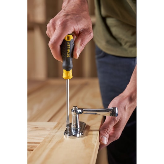 Photo of STANLEY STHT16146-0 screwdriver in use tightening a metal hinge on a wooden surface.