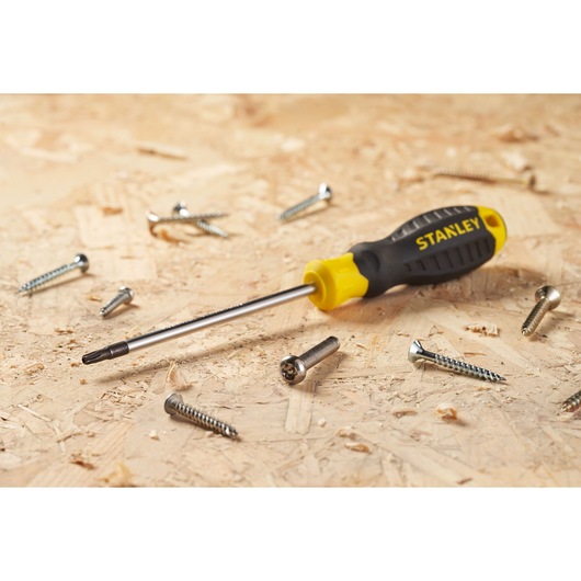 STANLEY STHT16179-0 screwdriver with black and yellow handle on wood surface, surrounded by metal screws, side angle.