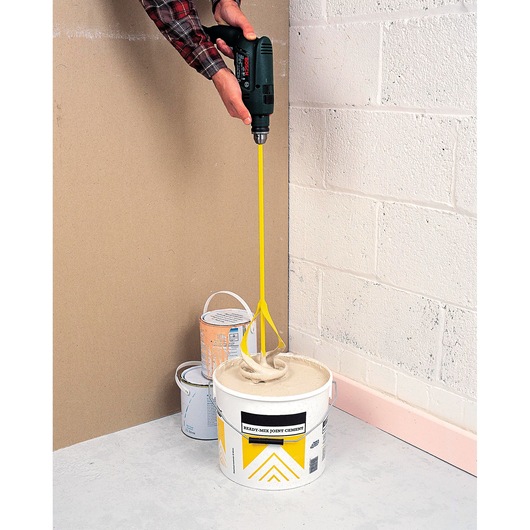 STANLEY STHT2-28043 yellow mixer tool mixing cement in bucket, photographed from above side angle.