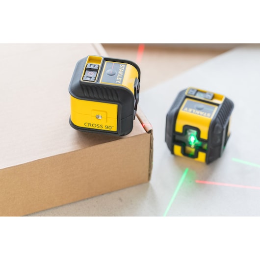 STANLEY STHT77502-1 yellow and black cross line laser level, two units on surfaces emitting green and red lines.