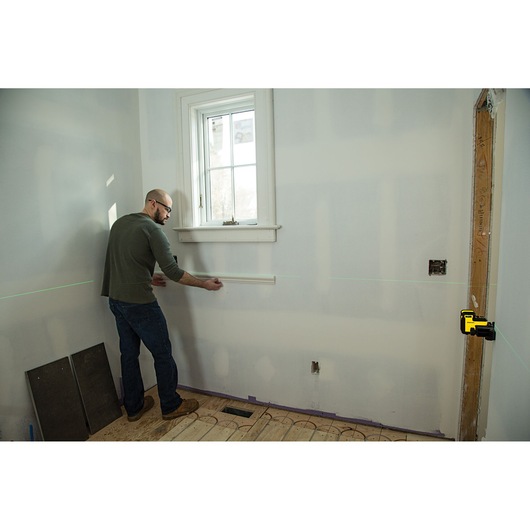 Photo of STANLEY STHT77594-1 laser level projecting green line on wall, person aligning trim in room.