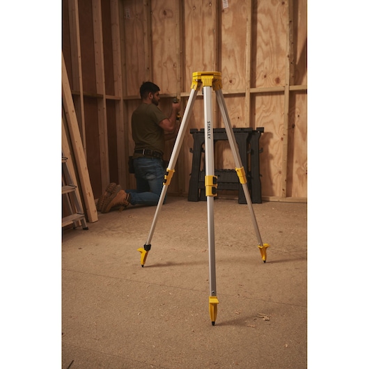 STANLEY STHT77625-1 tripod stand with yellow accents, positioned in a wooden construction room.