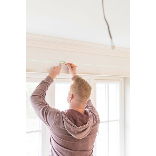 Photo of STANLEY STHT77641-1 laser level projecting green line on wall above window, person marking measurements.