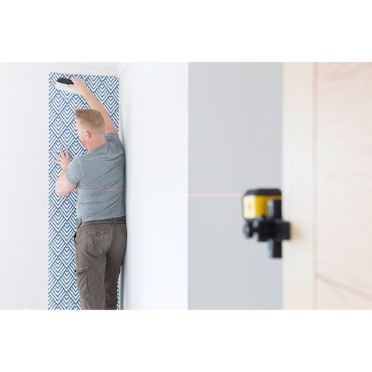 STANLEY STHT77648-1 laser level projecting red line, used for wallpaper alignment in a room.