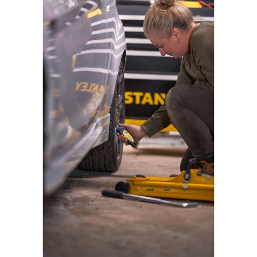 STANLEY STHT80874-0 digital tire pressure gauge used on car tire, close-up, tool in hand, yellow and black.