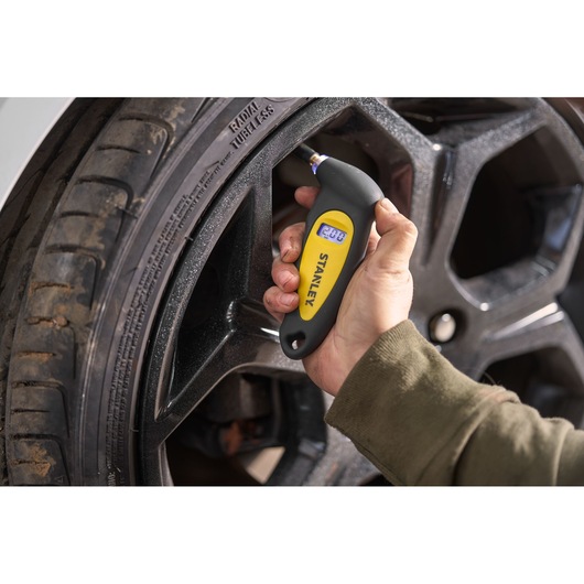 STANLEY STHT80874-0 digital tire pressure gauge checking car tire, close-up photography.
