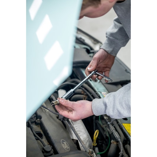 STANLEY STHT81583-0 ratchet tool used to remove a spark plug from a car engine, close-up photography.