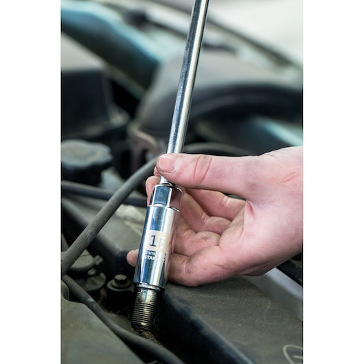 Photo of STANLEY STHT81583-0 spark plug socket being held by hand in automotive engine.