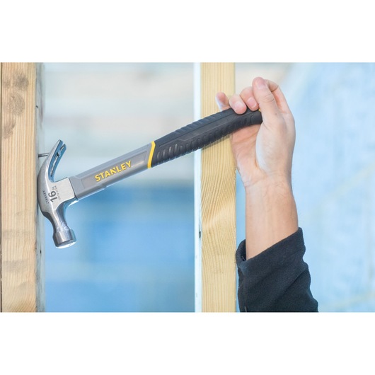 Photo of STANLEY STHT9-51309 claw hammer in use, black and yellow handle, striking nail into wood.