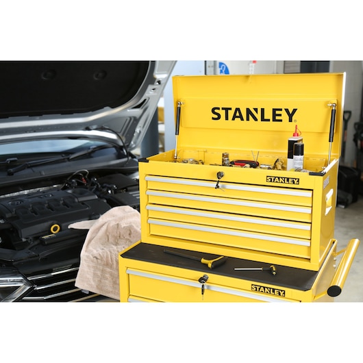 STANLEY STMT1-75062 yellow tool chest with open lid, drawers, and tools, photographed in a garage near a car.