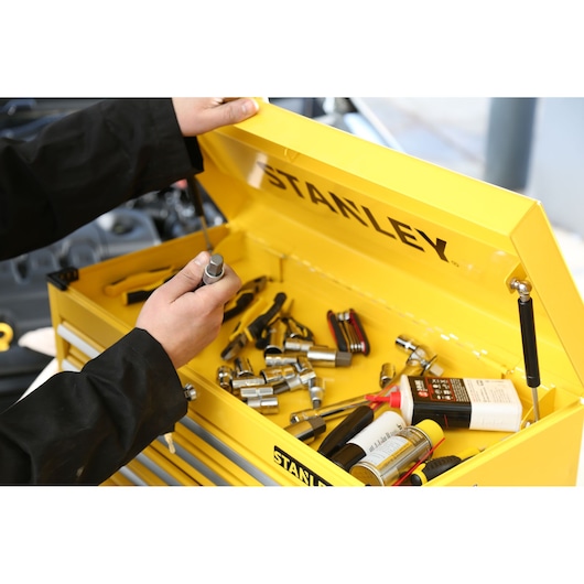 STANLEY STMT1-75062 yellow tool chest with assorted tools and lubricants, top compartment open, hands visible.