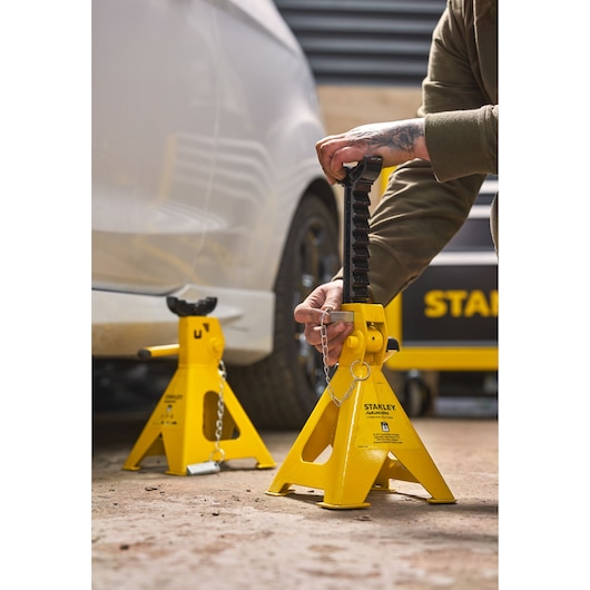 STANLEY STMT81255-1 yellow automotive jack stands in use near vehicle, outdoor setting.