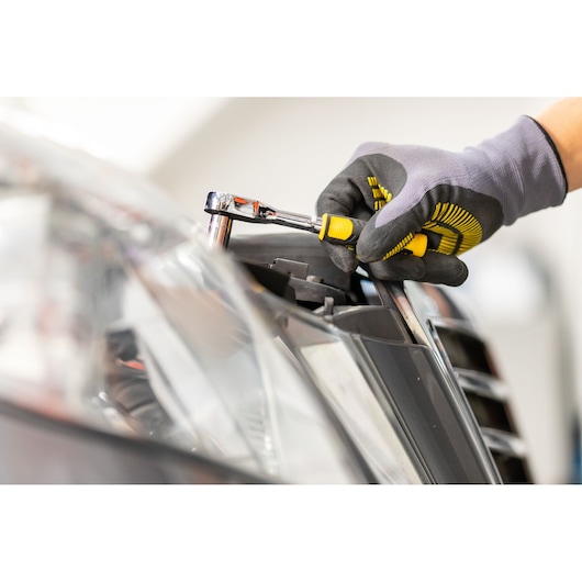 STANLEY STMT82672-0 ratchet set used on car headlight, close-up, showing tool grip and yellow details.