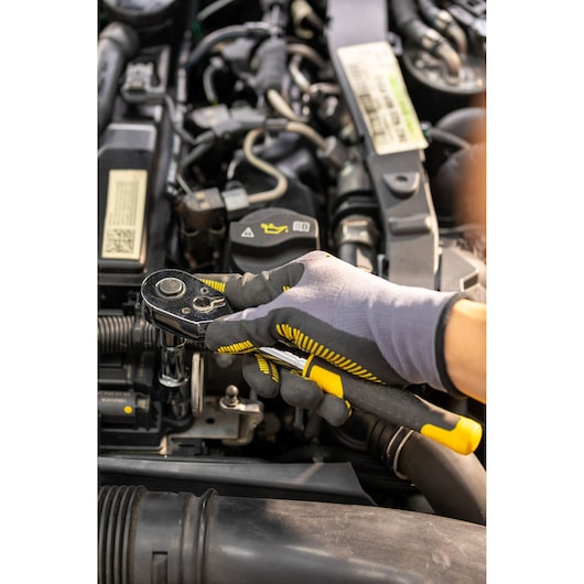 STANLEY STMT82830-1 ratchet wrench held by gloved hand, automotive engine maintenance.