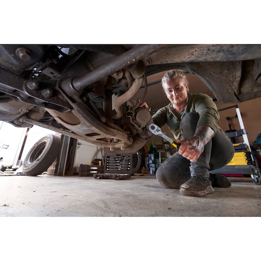 STANLEY STMT82831-1 ratchet in use under vehicle, tool set visible in workshop background.