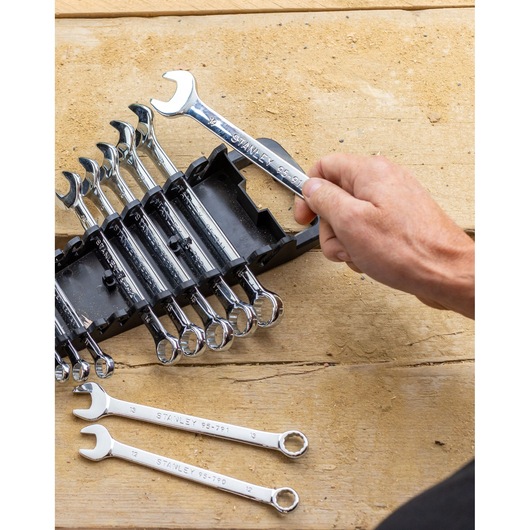 STANLEY STMT82842-0 wrench set in black holder, hand holding one chrome wrench, two wrenches on wooden surface.