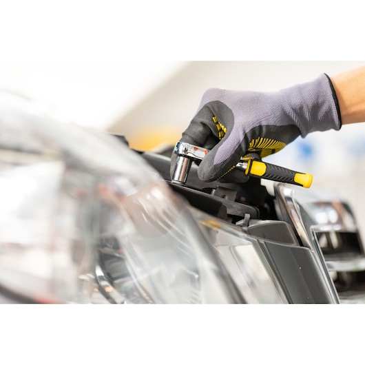 STANLEY STMT86105-0 ratchet handled by gloved hand near car headlight, close-up photography.
