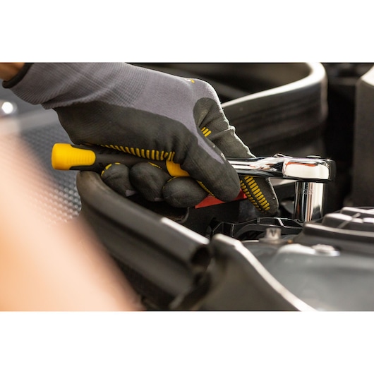 Photo of STANLEY STMT86307-0 ratchet wrench in use, close-up of gloved hand turning tool on engine.
