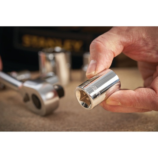 STANLEY STMT86527-0 chrome socket held by hand with ratchet wrench in background, close-up photography.