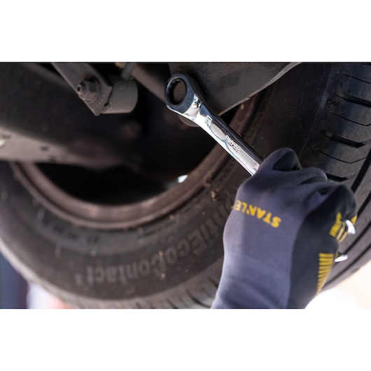 Photo of STANLEY STMT89909-0 ratcheting wrench being used on a car wheel bolt by a gloved hand.
