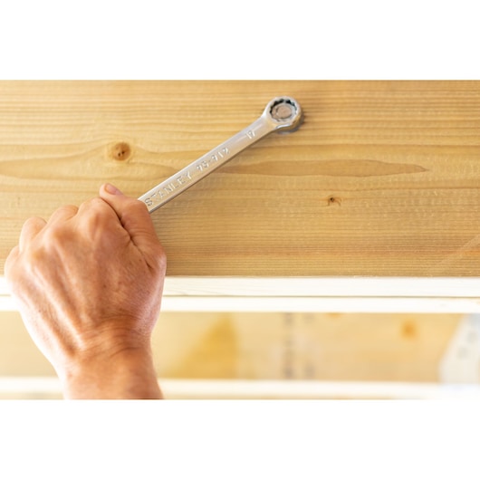 Photo of STANLEY STMT95912-0 ratcheting wrench in use on wood surface, close-up, hand holding tool.