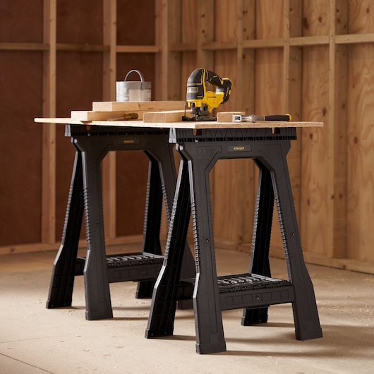 STANLEY STST1-70355 black plastic sawhorses used as workbench, side angle, in workshop setting.