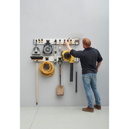 Photo of STANLEY STST22000-1 wall-mounted tool organizer with garden tools and a person arranging items.