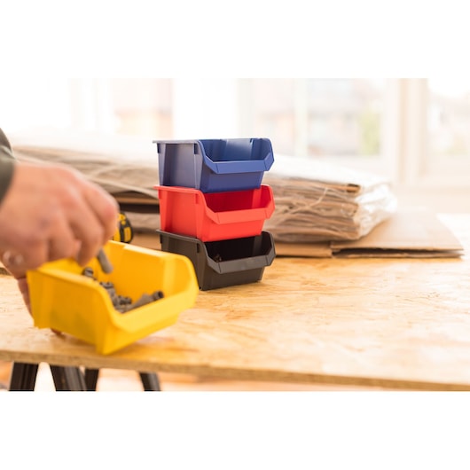 STANLEY STST82737-1 stackable plastic storage bins in blue, red, black, and yellow on a workshop table.