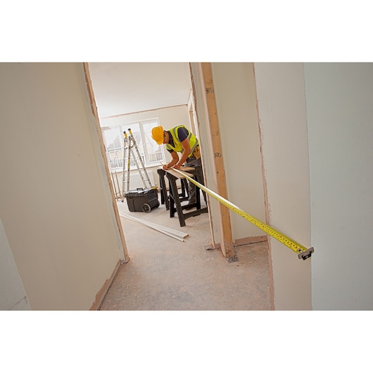 STANLEY XTHT0-33501 tape measure used by worker in construction site, yellow color, extended across doorway.