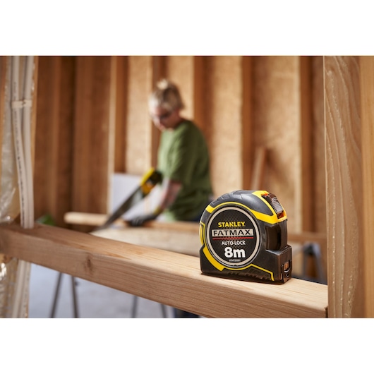 STANLEY XTHT0-33501 tape measure, black and yellow, on wood beam, FATMAX 8m Auto-Lock, construction setting.